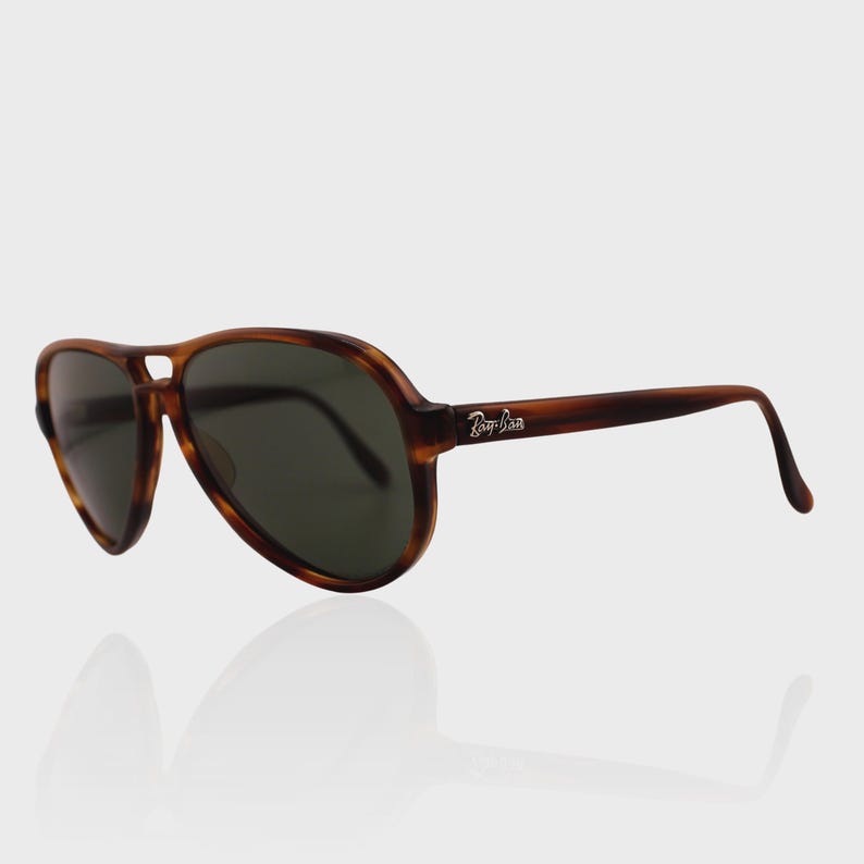 May include: Aviator sunglasses featuring a brown tortoiseshell frame and dark green lenses. The temples display the white Ray-Ban logo. These sunglasses have a classic teardrop shape with a double bridge design, providing a distinct look.