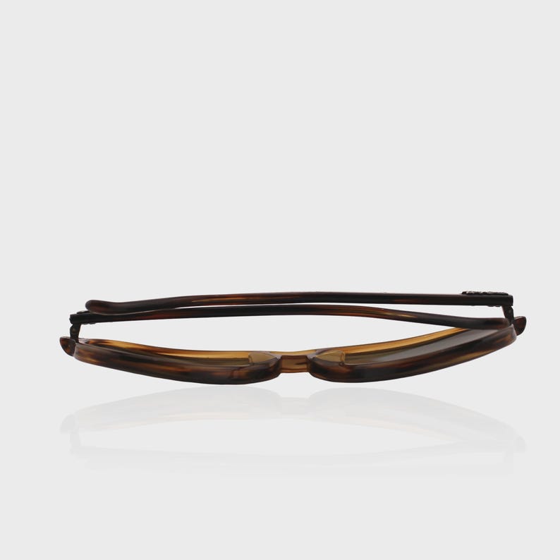 May include: Folded eyeglasses featuring a classic tortoiseshell pattern in shades of brown and amber. The frame is constructed with a bridge and two temples that are collapsed inward, showcasing the smooth, curved edges of the eyewear design.