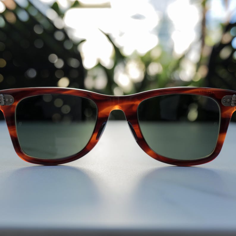May include: Tortoiseshell-patterned sunglasses with a classic rectangular frame shape. The frames feature a brown and amber marbled design with silver-toned metal accents at the hinges. The lenses are dark green and provide full coverage.