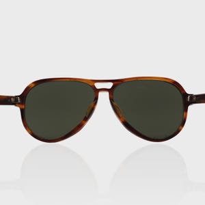 May include: Aviator sunglasses featuring a brown tortoiseshell pattern frame with a double bridge design and dark green tinted lenses. The eyewear has a classic teardrop shape with metal hinges connecting the temples to the front frame.
