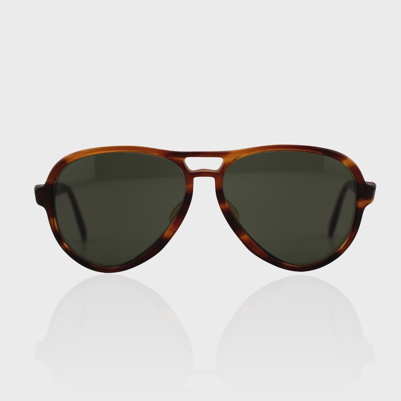 May include: Aviator sunglasses featuring a brown tortoiseshell pattern frame with a double bridge design and dark green tinted lenses. The eyewear has a classic teardrop shape with thick rims and curved temples extending from the sides of the frame.