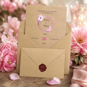 May include: A tan kraft paper wedding invitation card and matching envelope. The card features a pink floral wreath graphic, the text "Please join us to celebrate the wedding of: Aaroon & Olivia", and the date "Saturday April 26 2025 at 08:00 PM".