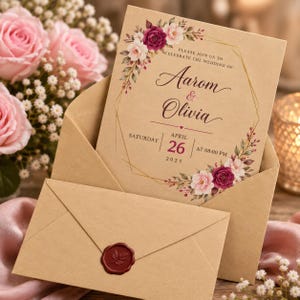 May include: A tan wedding invitation card featuring a gold geometric frame, floral illustrations in shades of burgundy and pink, and text reading: Please join us to celebrate the wedding of: Aarom & Olivia, Saturday, April 26, 2025, at 08:00 PM.