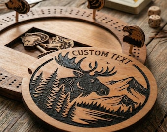Peut inclure: Jeu de cribbage en bois avec des chevilles en forme d'animaux, des dés et un jeu de cartes. Le plateau présente un design circulaire avec un orignal sculpté et les mots "CUSTOM TEXT". Les chevilles sont en forme d'ours, de loup et d'aigle.