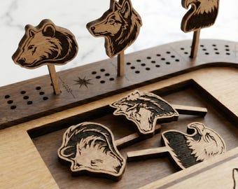 Peut inclure: Jeu de société en bois avec des pièces en forme d'animaux. Le jeu présente un ours, un loup et un aigle, avec des pièces supplémentaires éparpillées sur le plateau. Le plateau a une finition en bois foncé avec un cadre en bois clair.