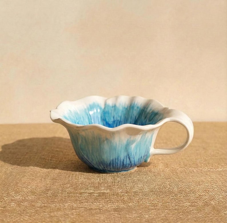 Puede incluir: Una taza de t&eacute; de cer&aacute;mica con borde ondulado y asa. La taza presenta un degradado de tonos azules, que van del blanco en el borde a un azul m&aacute;s profundo en la base. La taza tiene unos 10 cm de di&aacute;metro.