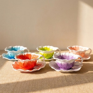 Puede incluir: Un juego de cinco tazas y platillos de cer&aacute;mica. Cada taza y platillo est&aacute; pintado de un color diferente: azul, naranja, verde, morado y melocot&oacute;n. Las tazas tienen un dise&ntilde;o de p&eacute;talo, y los platillos coinciden con los colores de las tazas.