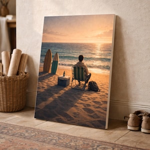 May include: A canvas print depicts a serene beach scene at sunset. A person sits in a folding chair, facing the ocean. Two surfboards lean on the sand. A cooler and a bottle sit nearby. The sky is a blend of orange and yellow.