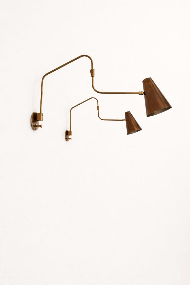 Puede incluir: Dos apliques de pared ajustables con una est&eacute;tica vintage. Las l&aacute;mparas presentan un acabado de lat&oacute;n con pantallas c&oacute;nicas en un tono cobre c&aacute;lido. El dise&ntilde;o incluye brazos articulados para iluminaci&oacute;n direccional.