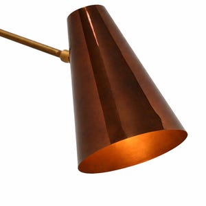 Puede incluir: Una pantalla de l&aacute;mpara en forma de cono de color cobre con un interior dorado y un brazo dorado. La pantalla de la l&aacute;mpara est&aacute; inclinada hacia abajo y el interior est&aacute; iluminado. La l&aacute;mpara es de dise&ntilde;o moderno.