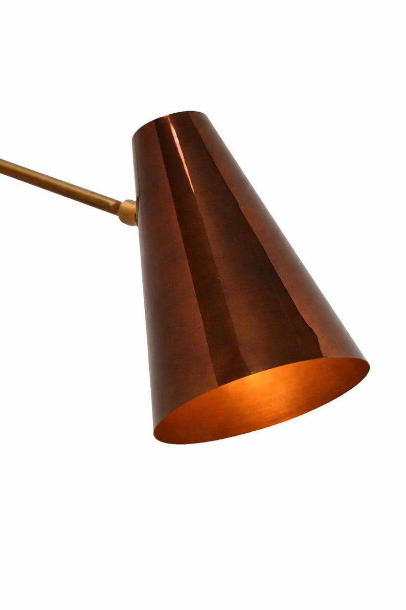 Puede incluir: Una pantalla de l&aacute;mpara en forma de cono de color cobre con un interior dorado y un brazo dorado. La pantalla de la l&aacute;mpara est&aacute; inclinada hacia abajo y el interior est&aacute; iluminado. La l&aacute;mpara es de dise&ntilde;o moderno.