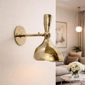 May include: A brass wall sconce with a conical shade and a cylindrical arm. The sconce is mounted on a round backplate. The shade has a series of small, evenly spaced holes. The fixture is a warm gold color.