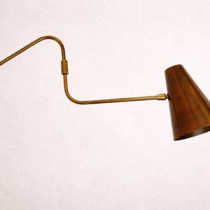 Puede incluir: Una l&aacute;mpara de pared de estilo vintage, con acabado en lat&oacute;n. Presenta un brazo largo y curvado y una pantalla c&oacute;nica en un tono cobre c&aacute;lido. El dise&ntilde;o es minimalista y elegante, adecuado para varios estilos de interior.