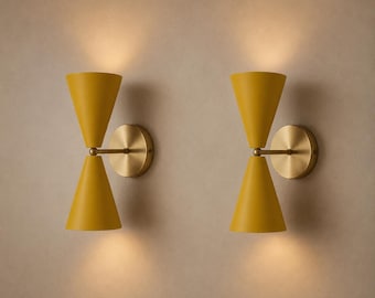 May include: A pair of wall sconces featuring two mustard yellow cone-shaped shades arranged in an hourglass configuration. Each fixture is mounted to the wall with a circular brass-toned plate and emits light from both the top and bottom cones.