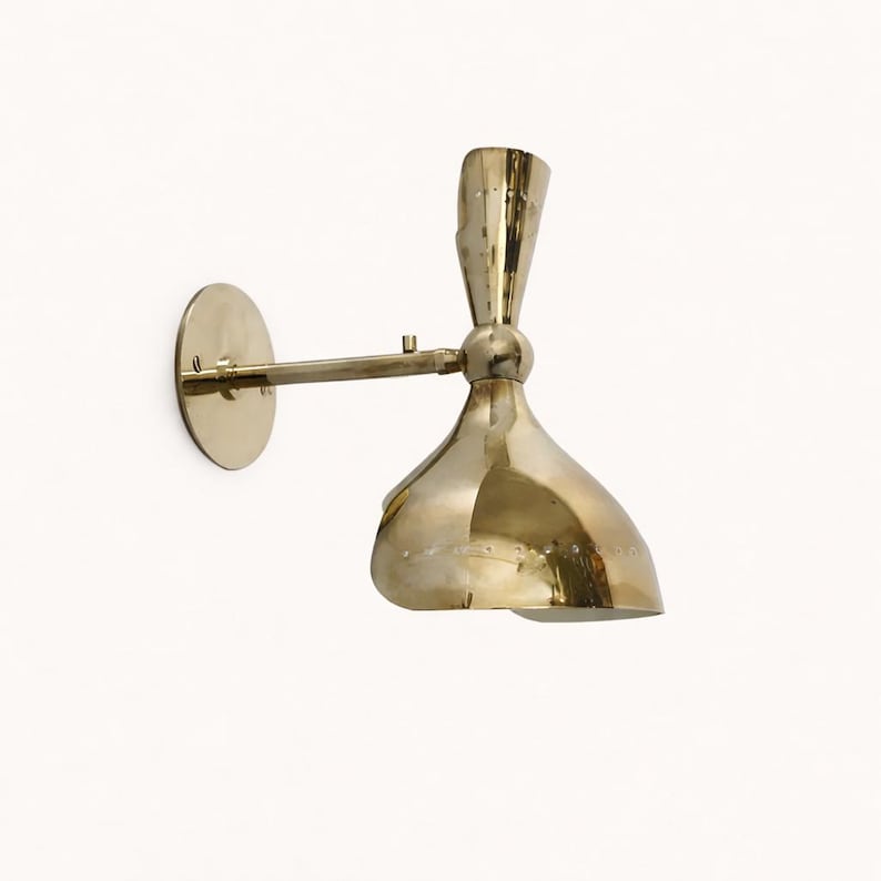 May include: A brass wall-mounted sconce with a round backplate, an adjustable arm, and a bell-shaped shade. The sconce has a polished finish and is designed for indoor lighting. The shade is approximately 6 inches in diameter.