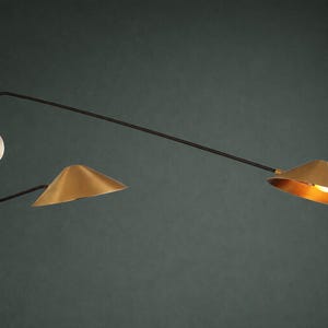 May include: Contemporary wall light with a brass finish and black arm. It has two conical shades and a circular wall mount. The light is set against a dark green background.