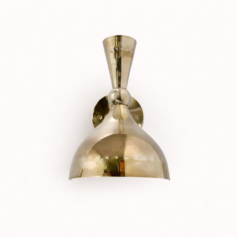 May include: A brass-colored wall sconce with a conical top and a rounded, bell-shaped shade. The sconce is mounted on a circular base and features a series of small, decorative rivets. The design is vintage and elegant.