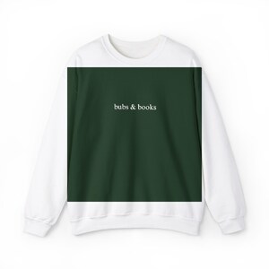 Puede incluir: Sudadera blanca y verde oscuro con el texto "bubs & books" en blanco. La sudadera tiene mangas blancas y un panel frontal verde oscuro. El texto está centrado en el panel frontal.