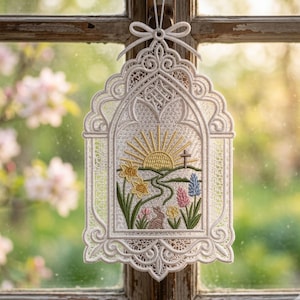 May include: An Easter-themed window hanging with a white lace design. It depicts a sunrise, a cross, and a path with flowers and a bunny. The ornament is suspended by a white ribbon, creating a delicate and festive decoration.