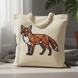 May include: A beige tote bag with a geometric fox design in orange, brown, black, and white. The fox is depicted in a standing pose with an angular pattern. The bag has matching beige handles.