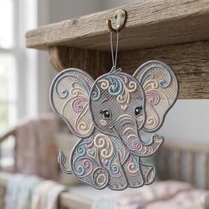 K&ouml;nnte beinhalten: Gesticktes Elefanten-Ornament in Grau mit pastellblauen, rosa und cremefarbenen Akzenten. Der Elefant hat ein detailliertes Wirbeldesign und h&auml;ngt an einem Messinghaken. Das Ornament ist wahrscheinlich f&uuml;r ein Kinderzimmer.