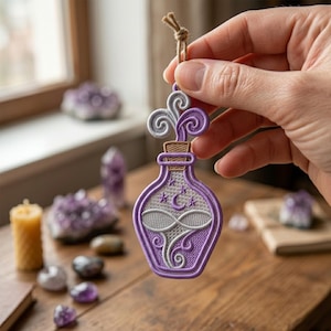 May include: A purple embroidered potion bottle ornament with a cork stopper and swirling steam. The bottle features a crescent moon and star design. A brown string is attached for hanging. The background includes crystals and a candle.