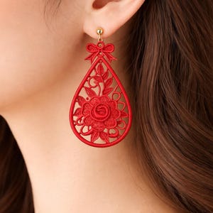 Puede incluir: Pendientes rojos en forma de lágrima con diseño floral. Los pendientes presentan un lazo en la parte superior y un patrón calado detallado. Los pendientes son de material rojo y tienen un perno dorado.