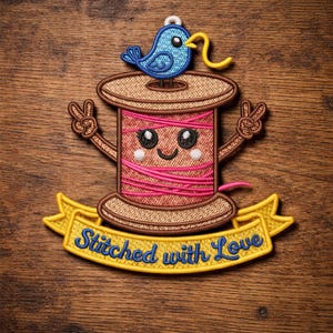 Könnte beinhalten: Gestickter Aufnäher mit einer lächelnden Spule aus rosa Faden mit einem blauen Vogel oben. Der Aufnäher hat braune, gelbe und blaue Akzente und ein gelbes Banner mit dem Text "Stitched with Love".