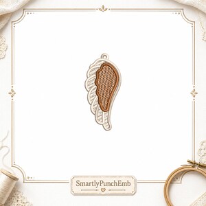 May include: Embroidered wing design with a textured brown center, outlined in tan and white. The wing has a loop at the top for hanging. The design is set against a white background with a decorative border. The text "SmartlyPunchEmb" is at the bottom.