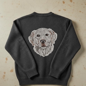 May include: Dark gray sweater featuring an embroidered dog face on the back. The dog's face is detailed with shades of gray, brown, and white, creating a realistic and textured appearance. The sweater has a ribbed crew neck and cuffs.