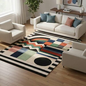May include: A modern living room featuring a colorful geometric patterned rug with black and white stripes. The rug is placed in front of a white sofa and two armchairs. The room has hardwood floors and a large window.