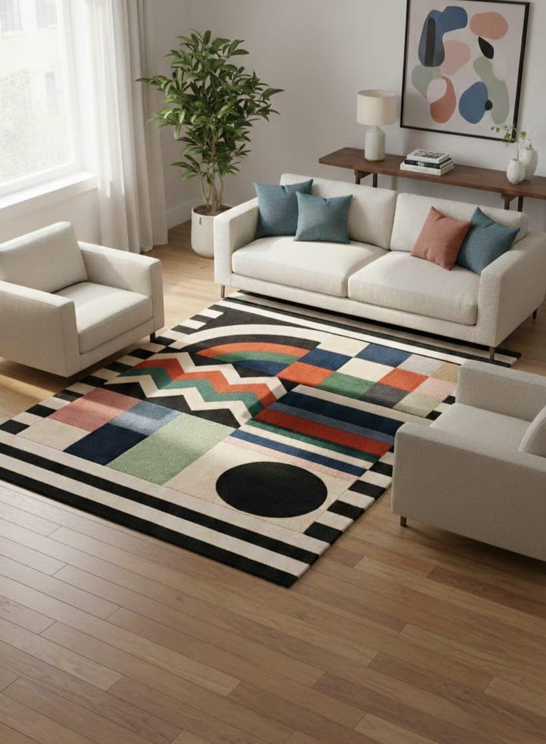 May include: A modern living room featuring a colorful geometric patterned rug with black and white stripes. The rug is placed in front of a white sofa and two armchairs. The room has hardwood floors and a large window.