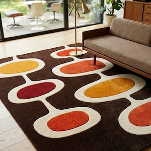 May include: A brown mid-century modern rug with an abstract pattern of connected ovals in orange, yellow, and red, outlined in white. The rug is placed in a living room with a brown sofa and a brass floor lamp.