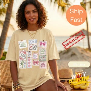 May include: A light yellow t-shirt featuring various Mahjong tile designs and the text "MAHJ". Other graphics include pink bows and the text "ONE MORE GAME". The shirt is a comfort colors style.