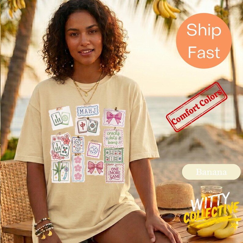 May include: A light yellow t-shirt featuring various Mahjong tile designs and the text "MAHJ". Other graphics include pink bows and the text "ONE MORE GAME". The shirt is a comfort colors style.