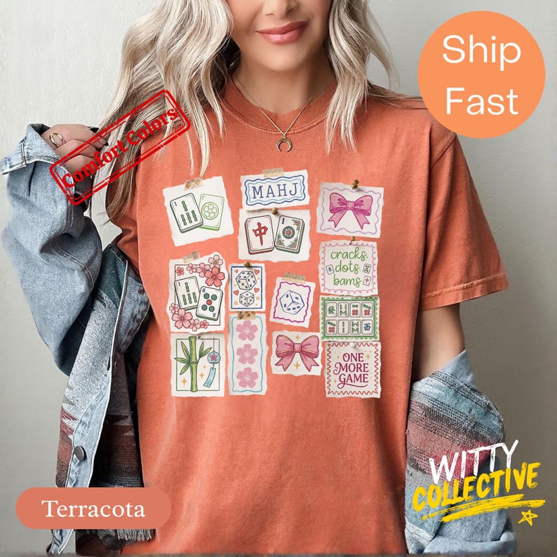 May include: Terracotta-colored t-shirt featuring a collage of Mahjong tile illustrations, pink bows, and floral accents. The shirt includes the text "MAHJ" and "ONE MORE GAME".