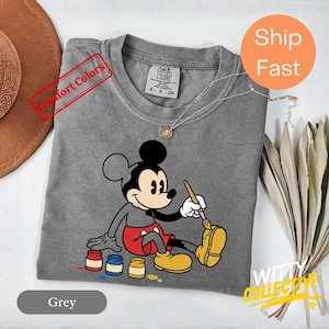 May include: A set of three ceramic mugs with a speckled, matte finish. The mugs are in shades of cream, light gray, and dark gray. Each mug has a simple, minimalist design and a rounded handle.