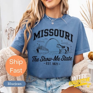 Puede incluir: Camiseta azul con un gr&aacute;fico negro del arco de Missouri, un caballo y un barco. El texto "MISSOURI" est&aacute; encima del gr&aacute;fico, y "The Show-Me State - EST. 1821-" est&aacute; debajo. La camiseta es de manga corta y cuello redondo.