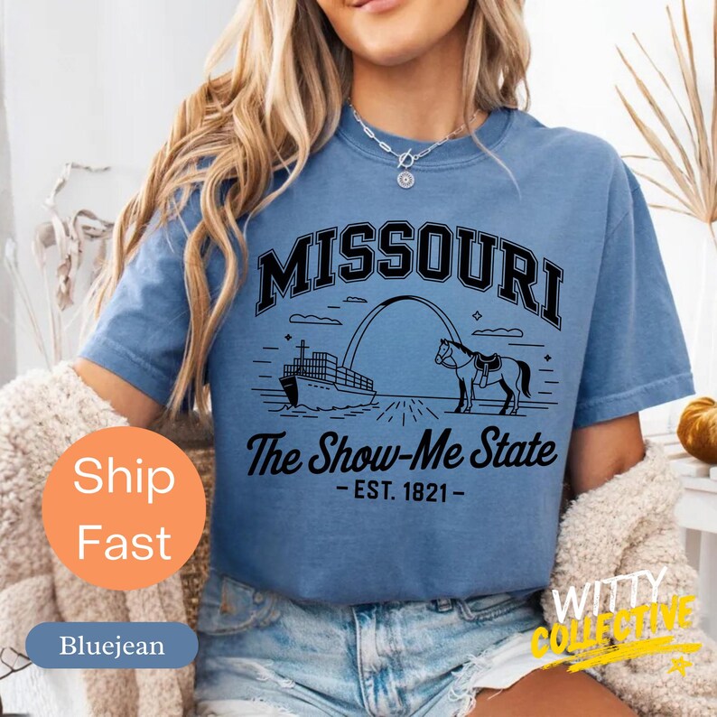 Puede incluir: Camiseta azul con un gr&aacute;fico negro del arco de Missouri, un caballo y un barco. El texto "MISSOURI" est&aacute; encima del gr&aacute;fico, y "The Show-Me State - EST. 1821-" est&aacute; debajo. La camiseta es de manga corta y cuello redondo.