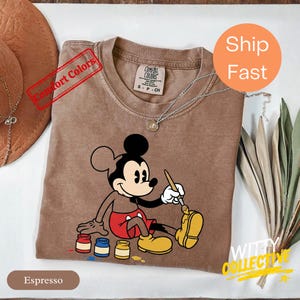 May include: A white ceramic mug with a black handle and the text "But First, Coffee" in a bold, black font. The mug is set against a blurred background, suggesting a cozy setting. The mug appears to be approximately 4 inches tall.