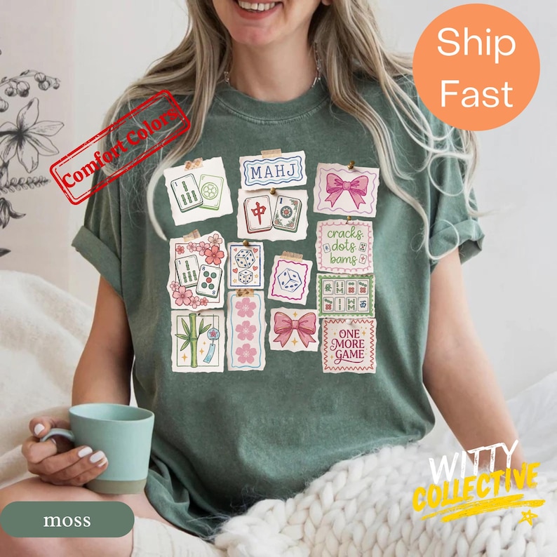 May include: Moss green t-shirt featuring a collage of Mahjong tile illustrations, pink bows, and the text "ONE MORE GAME." The shirt has a relaxed fit and the words "Comfort Colors" are printed on the top left.