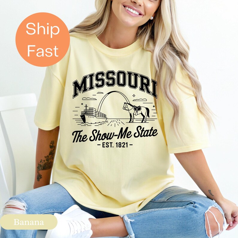 Puede incluir: Camiseta amarillo claro con la palabra "MISSOURI" en letras negras. Debajo, un gr&aacute;fico de un barco, un caballo y el texto "The Show-Me State - EST. 1821-". La camiseta es de corte holgado.
