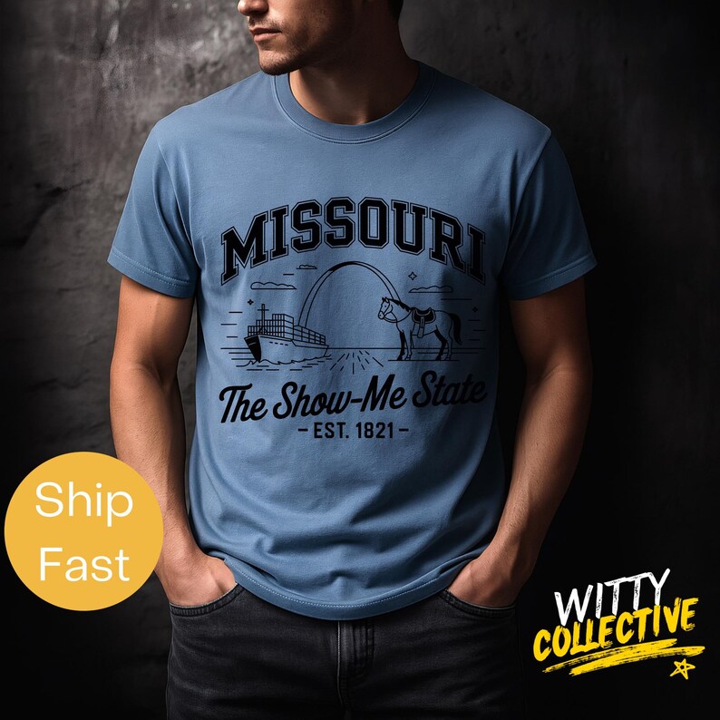 Puede incluir: Camiseta azul claro con un dise&ntilde;o gr&aacute;fico negro. El dise&ntilde;o incluye la palabra "MISSOURI" encima de una ilustraci&oacute;n de un barco, un arco y un caballo, con el texto "The Show-Me State - EST. 1821-" debajo. La camiseta la lleva una persona.