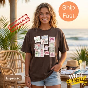 May include: Espresso-colored t-shirt featuring a collage of Mahjong tile illustrations and text. The design includes pink bows, floral elements, and the word "MAHJ". The shirt is a comfort color and is part of the Witty Collective.