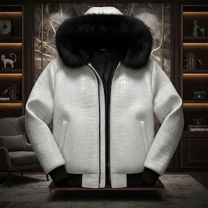 Könnte beinhalten: Eine weiße Jacke mit Krokodilleder-Muster und einer schwarzen, pelzgefütterten Kapuze. Die Jacke hat einen Reißverschluss und schwarze Manschetten. Das Design ist strukturiert. Die Jacke wird auf einer dunklen Oberfläche präsentiert.