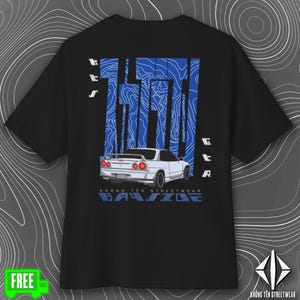 May include: Black t-shirt featuring a white car graphic with red taillights, set against a blue abstract design. The shirt includes the text "GTA" and "KHÔNG TÊN STREETWEAR" in blue and white. The design is centered on the back of the shirt.