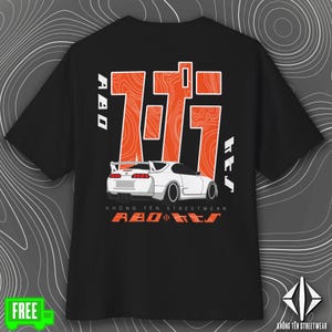 May include: Black t-shirt featuring a white sports car graphic with orange accents and Japanese characters. The shirt includes the text "KHÔNG TÊN STREETWEAR" and "ABO KES" in orange. A green "FREE" sticker is in the lower left corner.