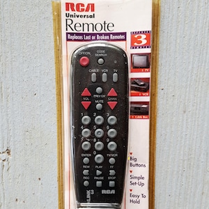 May include: RCA universal remote control in its original packaging. The black remote has red and gray buttons and is designed to replace lost or broken remotes. The packaging highlights features like big buttons and easy setup.