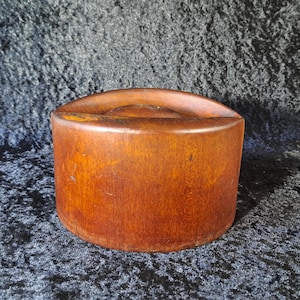 May include: A cylindrical wooden box with a curved top. The box is made of a warm, reddish-brown wood and has a smooth, polished finish. The box is likely used for storage or display.