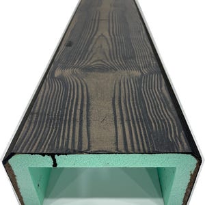 May include: A dark brown, rectangular faux wood beam with a light green interior. The wood grain pattern is visible on the top surface. The beam has a hollow, open bottom.